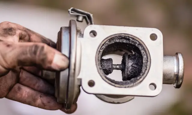 Brudny zawór EGR z nagarem. Ręce mechanika pokryte sadzą.