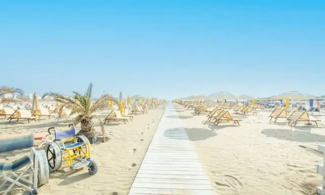 Una passerella bianca conduce alle spiagge di Riccione, con sdraio e ombrelloni pronti per accogliere tutti, compresa una sedia a rotelle speciale per la sabbia.