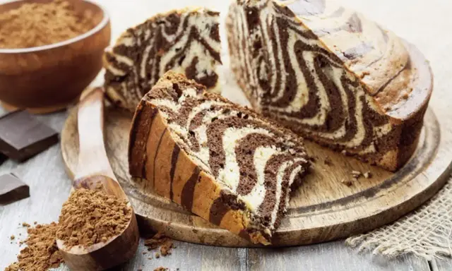 Wilgotne ciasto zebra z czekoladowymi i waniliowymi pasami, pokrojone na plastry, obok kakao i czekolady.
