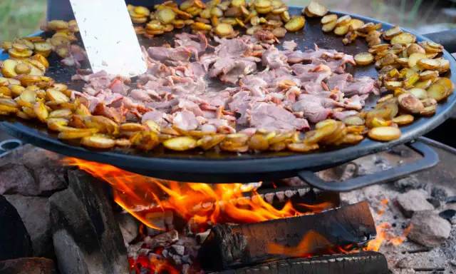 En stor stekpanna över öppen eld där kött och potatis tillagas. En perfekt dag att laga mat ute!