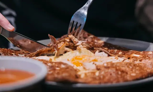 Une galette garnie d'œuf et de poulet, un délice des spécialités de Bretagne, est coupée avec un couteau et une fourchette.
