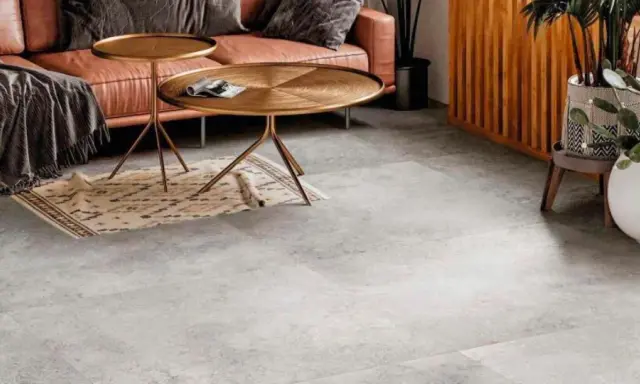 Un elegante soggiorno con divano in pelle color caramello, tavolini dorati e un tappeto etnico su un **pavimento grigio** che crea **abbinamenti** moderni e sofisticati.