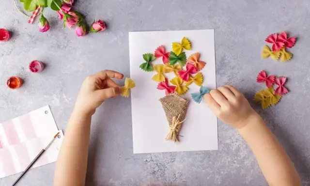Dziecko tworzy bukiet z kolorowego makaronu farfalle na laurce. Świetne pomysły na laurki!
