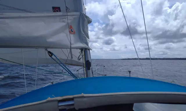 Vue depuis un voilier, le **lofer voile** blanc gonflé par le vent, sur une mer agitée sous un ciel nuageux.