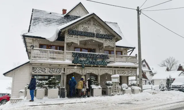Drewniana chata z napisem "Schronisko Smaków" i neonem "Restauracja" w Bukowinie Tatrzańskiej, otoczona śniegiem.