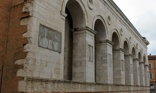 Archi maestosi e decorazioni in pietra della chiesa San Francesco a Rimini, con un muro in mattoni a vista che racconta la sua storia.