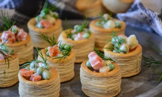 Plusieurs bouchées à la reine garnies d'une salade crémeuse de petits pois, carottes et saumon, décorées d'aneth.