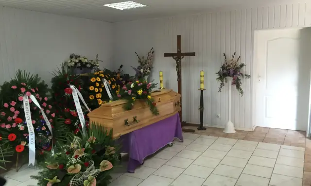 Drewniana trumna otoczona wieńcami i bukietami. Piękne kwiaty na trumnę tworzą smutną, ale uroczystą atmosferę.