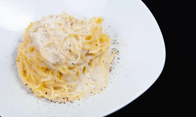Un piatto di spaghetti cacio e pepe, cremosi e ricchi, cosparsi di pepe nero macinato fresco e formaggio grattugiato.