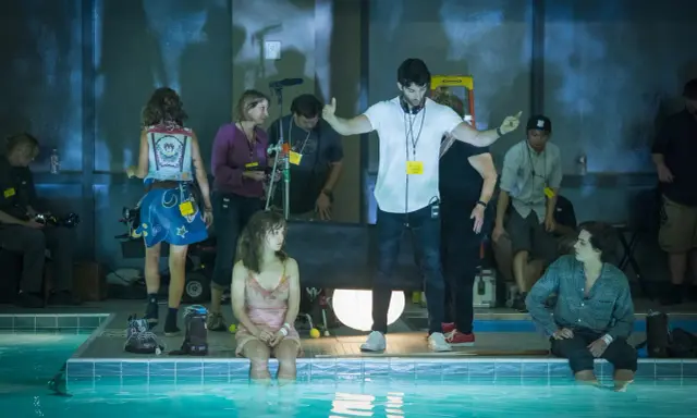 Reżyser instruuje aktorkę siedzącą w basenie. Wszyscy są **trzy kroki od siebie**, tworząc scenę filmową.