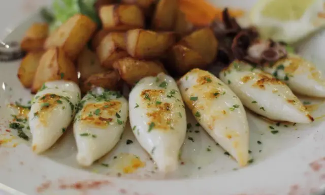 Chipirones a la plancha, tiernos y dorados, acompañados de patatas rústicas y un toque de perejil fresco.