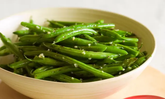 Fagiolini in padella conditi con aglio e pepe, serviti in una ciotola di legno.