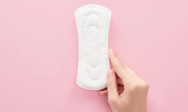 Una mano toca una compresa sobre fondo rosa. Representa cómo es el flujo antes de la regla, ligero y discreto.