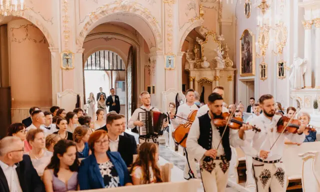 Muzycy grają piosenkę dla świadków w kościele. W tle para młoda wchodzi do świątyni.