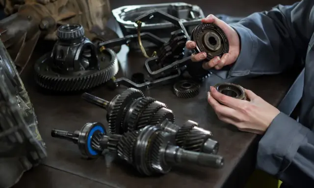 Mechanik analizuje części skrzyni biegów, szukając przyczyny, dla której sprzęgło skrzypi przy puszczaniu.