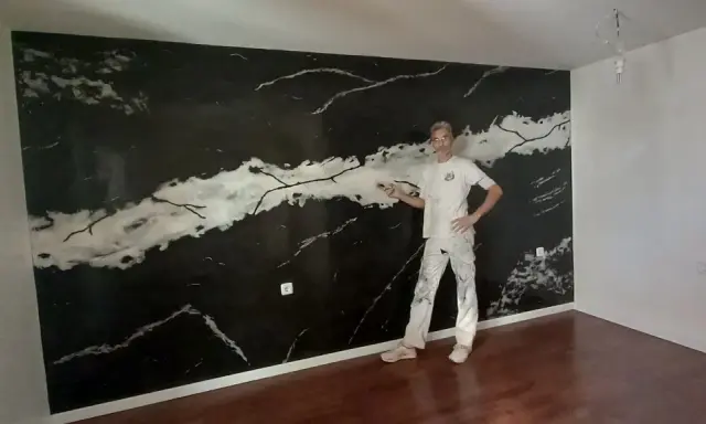 Pintor posa frente a una pared con falso estuco de mármol negro y blanco.