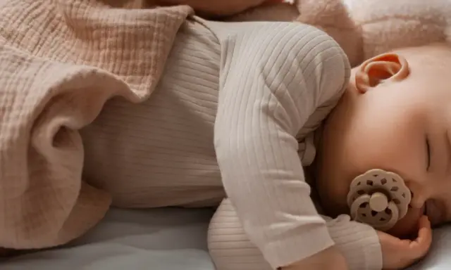 Un tenero neonato dorme sereno, avvolto in una copertina color pesca, con un ciuccio che lo culla nel sonno.