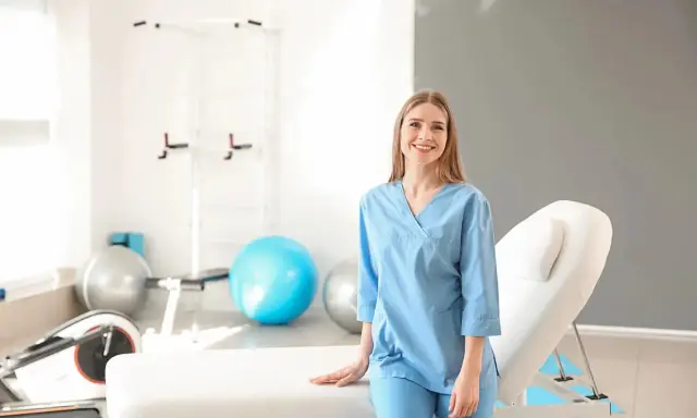 Uśmiechnięta fizjoterapeutka w gabinecie rehabilitacyjnym. Zastanawiasz się, ile zarabia fizjoterapeuta?