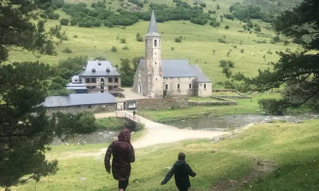 Dos niños corren por un sendero en un valle verde hacia una iglesia y casas de piedra. ¡Un plan perfecto de qué hacer en Vielha con niños!