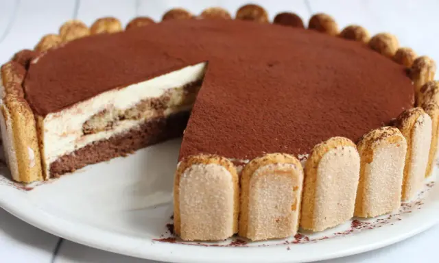 Eine köstliche tiramisu torte, mit Löffelbiskuits und Kakaopulver verziert, wartet darauf, angeschnitten zu werden.