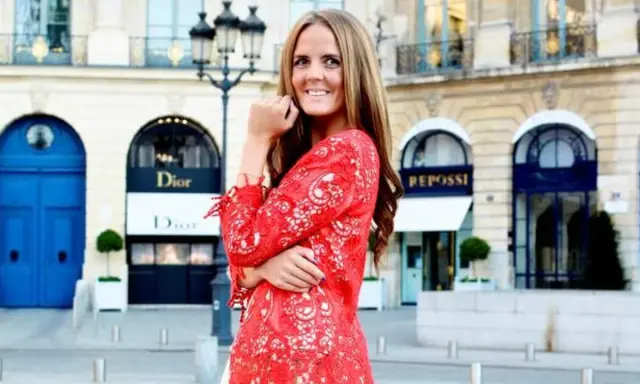 En kvinna i röd spetsklänning poserar framför Dior i Paris. Drömmer om ett jobb inom mode.