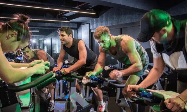 Intensywny trening spinningowy w grupie. Ludzie z determinacją pedałują na rowerach stacjonarnych, pocą się i walczą o każdy kilometr.