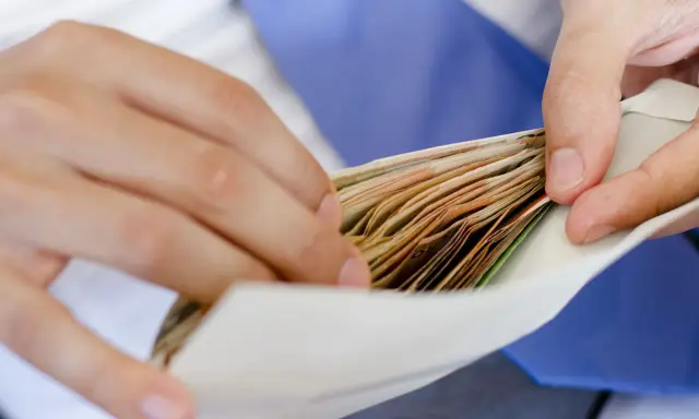 Dłonie wkładają plik banknotów do koperty na wesele.