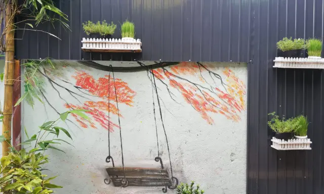 Un columpio pintado en un muro, ideal para inspirar al pintar patios pequeños. Las ramas anaranjadas y el bambú añaden color.