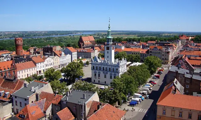 Urokliwy widok na rynek i zabytkowe kamieniczki w kujawsko-pomorskim. W tle rzeka i zieleń.