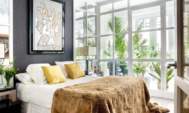 Un dormitorio moderno con cama mullida, arte abstracto y ventanales que invitan a diseña tu dormitorio con luz natural y plantas.