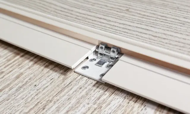 Détail d'une lame PVC qui se soulève, révélant une fixation métallique et des vis sur un parquet imitation bois.