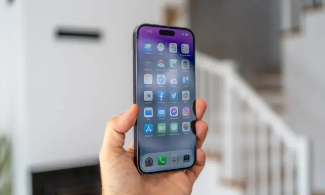 Dłoń trzyma smartfon z widocznym ekranem iPhone 14 Pro Max. Na wyświetlaczu widać ikony aplikacji i godzinę 11:02.