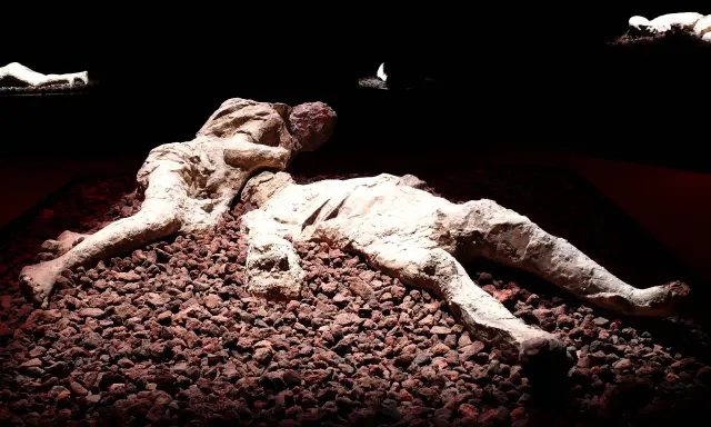 Pompeje zastygli ludzie w popiele, ostatnie chwile uwiecznione w kamieniu. Dwie postacie leżą obok siebie, otoczone gruzem.