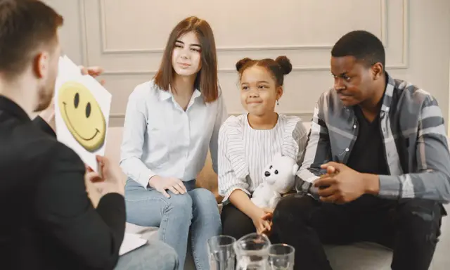 Familie spricht mit Therapeut. Ein Kind will nicht in die Schule, aber ein Smiley-Bild soll helfen.