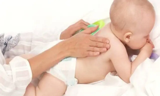 Delikatny masaż pleców niemowlaka, który waży już 9 kg. Ręce opiekuna głaszczą jego plecy.