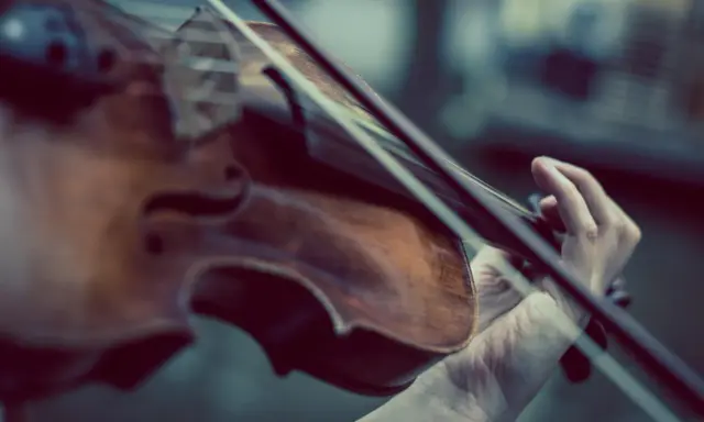 Main d'un musicien jouant du violon, un instrument à cordes, pas à vent. La musique s'élève.