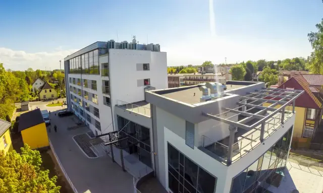 Nowoczesny budynek, gdzie hotel skal właściciel dba o komfort gości. Widać parking, zielone otoczenie i słoneczne niebo.