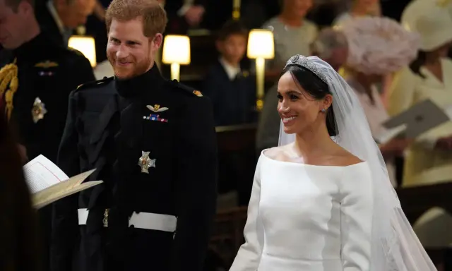 Meghan Markle y el Príncipe Harry sonríen en su boda. Ella luce un vestido blanco y él un uniforme militar.