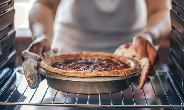 Hände mit Ofenhandschuhen nehmen einen frisch gebackenen Nusskuchen aus dem Ofen. Alles, was man zum Backen braucht: Zutaten, ein Rezept und Geduld.