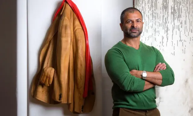 Livio De Marchi, artiste sculpteur, pose à côté de son manteau en bois sculpté, une œuvre saisissante.