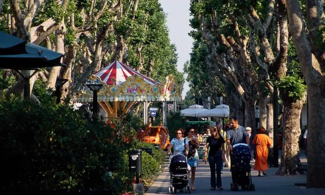 Passeggiata nel centro di Bellaria, con giostra, alberi maestosi e famiglie con passeggini.