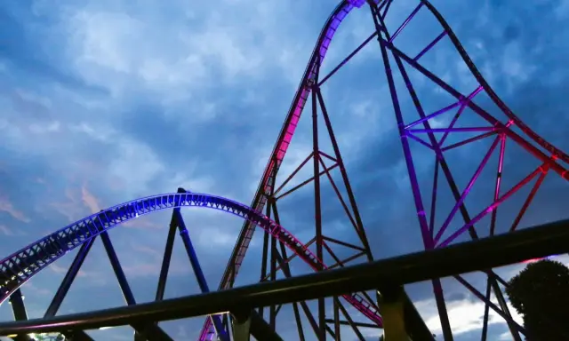 Najwyższy rollercoaster na świecie, oświetlony niebieskim i różowym światłem, wznosi się na tle burzowego nieba.