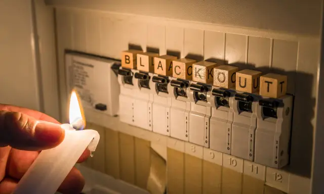 Płonąca świeca obok bezpieczników z literami układającymi się w słowo "blackout".