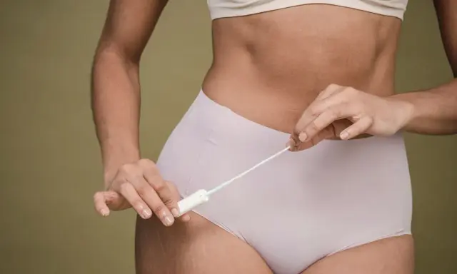 Kobieta trzymająca tampon, zastanawiająca się, czy okres się spóźnia.