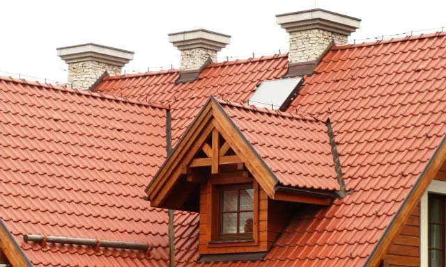 Dach dwuspadowy z czerwonej dachówki, z kominami i lukarną. Instalacja odgromowa zabezpiecza budynek.