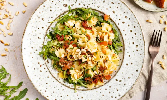 Ein köstlicher mediterraner Salat mit Farfalle, getrockneten Tomaten, Rucola und Pinienkernen.