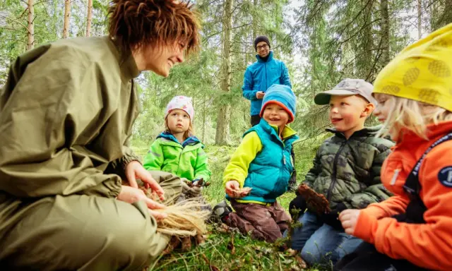 En grupp barn och en vuxen njuter av en dag i mulle skogen, omgivna av träd och grönskande natur.