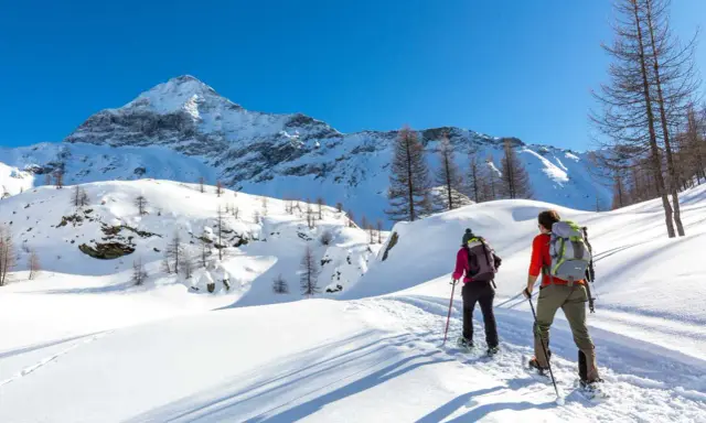 Coppia con ciaspole esplora un sentiero innevato in montagna, un'ottima idea per chi cerca dove ciaspolare in Lombardia.