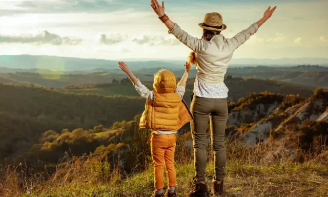 Bambini in Toscana, con le braccia al cielo, ammirano un paesaggio collinare al tramonto.