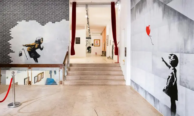Banksy Lissabon: ikonische Werke wie das Mädchen mit dem roten Ballon und die wegspritzende Frau zieren die Wände einer Ausstellung.